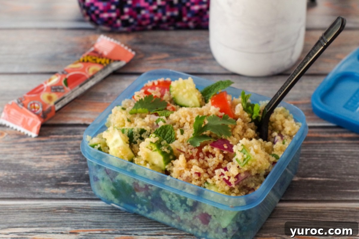 quinoa salad in a blue lunch container with plastic fork and lunch bag, water bottle and granola bar in the background