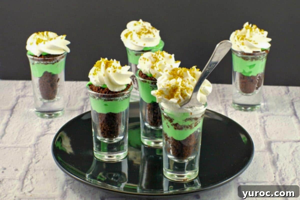 St. Patrick's Day Shamrock Irish Cream Shots 4 4 Shamrock St. Patrick's Day Irish Cream dessert shots on a black plate on a faux wood surface with 2 more in the background.