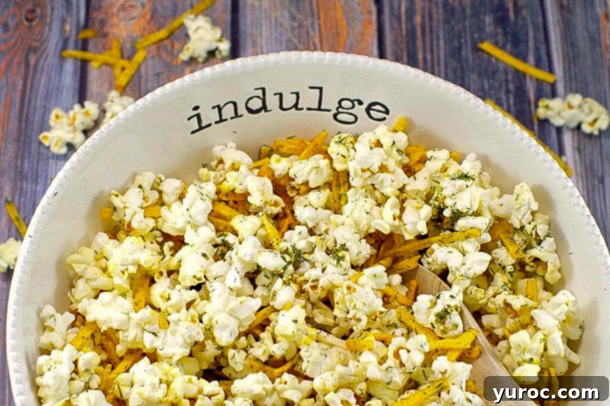 Savory popcorn in a white bowl, with the words 'indulge' on it, on faux wooden surface.