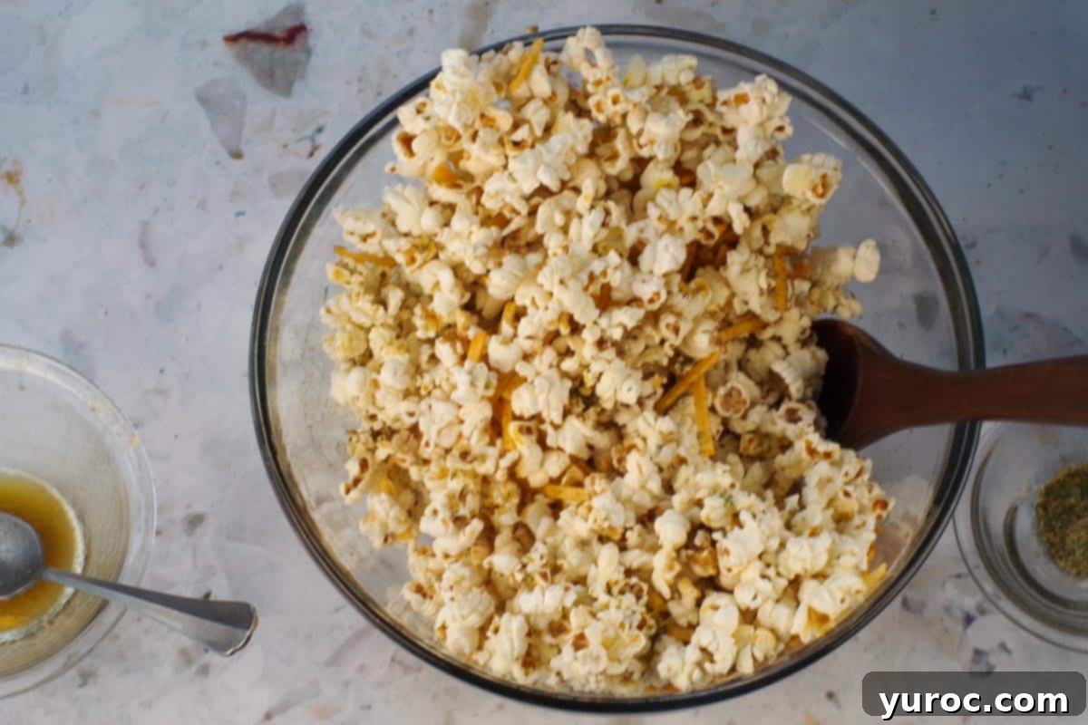 Popcorn in a large glass bowl being mixed with a wooden spoon.