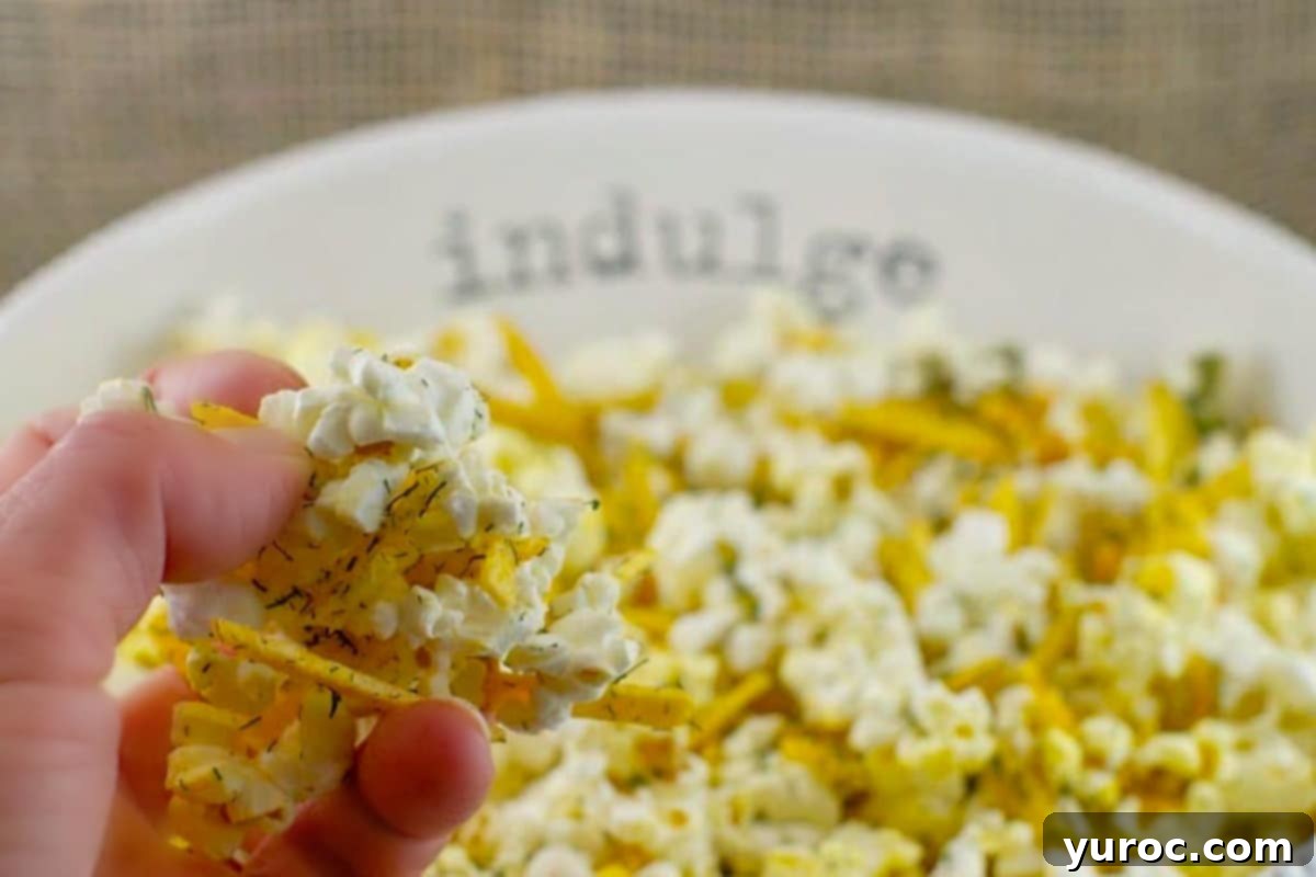 Savory popcorn in a white bowl, with the words 'indulge' on it, on faux wooden surface.