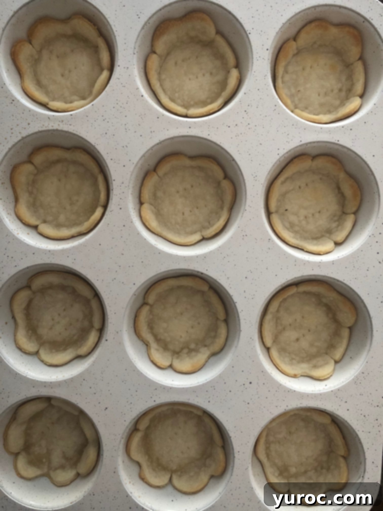 A muffin tin filled with perfectly baked, golden-brown tart shells cooling after being removed from the oven.