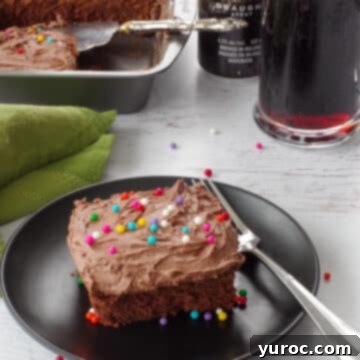 A perfectly sliced piece of chocolate Guinness cake resting on a black plate, with the remainder of the cake in its pan visible in the soft background, an ideal St. Patrick's Day dessert.