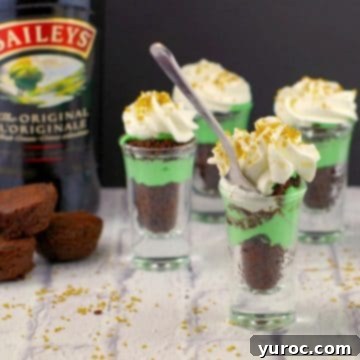 Vibrant Irish cream dessert shots presented with a bottle of Irish cream in the background, set on a crisp white faux surface, ready for a St. Patrick's Day celebration.