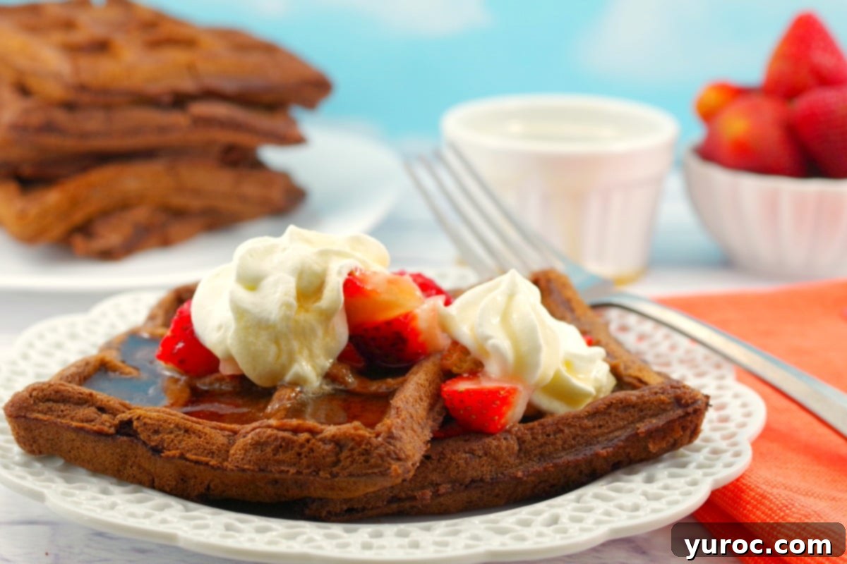 Decadent Belgian Chocolate Waffles 2 Belgian Chocolate Waffles topped with fresh berries and whipped cream on a white plate. A stack of waffles sits in the background.