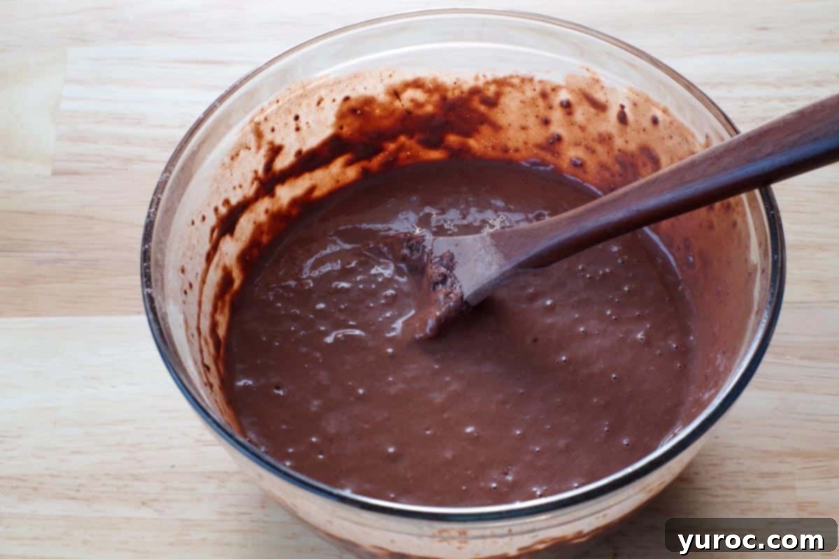 Decadent Belgian Chocolate Waffles 7 dry ingredients combined with egg yolk mixture in a glass bowl, with wooden spoon