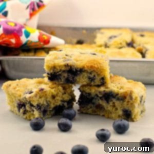 Wholesome Blueberry Cornbread Delight 16 Three pieces of healthy blueberry cornbread stacked on a counter with a pan of blueberry cornbread in background