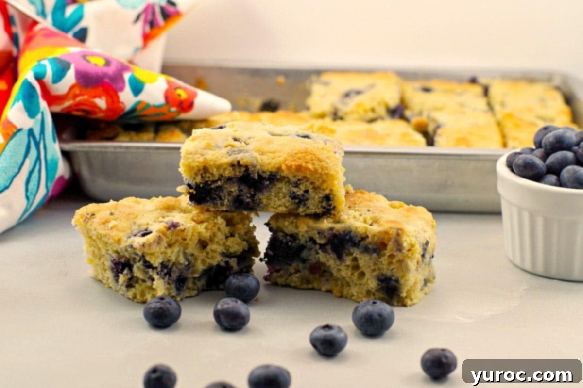 Wholesome Blueberry Cornbread Delight 4 Three perfectly sliced pieces of healthy blueberry cornbread stacked on a wooden counter, with a full pan of cornbread blurred in the background.