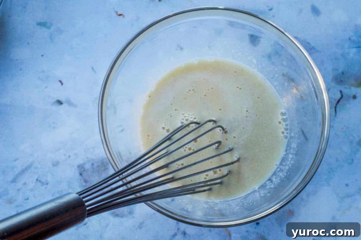 Wholesome Blueberry Cornbread Delight 8 Wet ingredients for cornbread (egg, milk, applesauce, vanilla) mixed together in a glass bowl with a whisk.