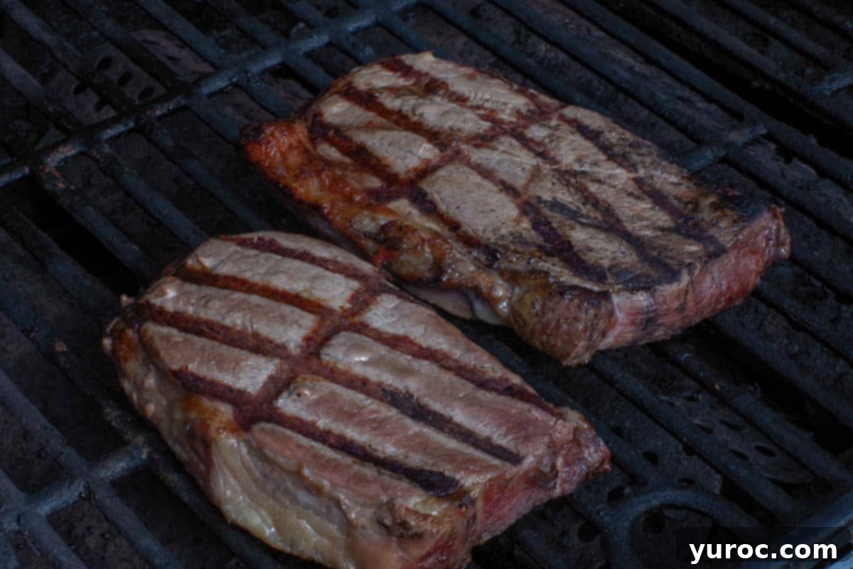 Two steaks grilling on a hot BBQ, smoke rising.
