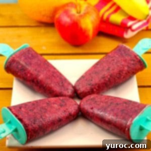 4 fruit popsicles on a white plate with fruit in background