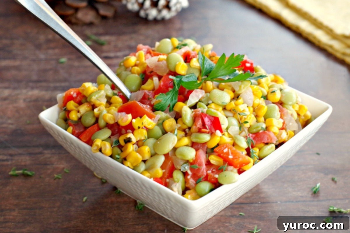 A bowl of vibrant corn succotash, garnished with fresh herbs, resting on a rustic wooden surface with decorative pine cones in the soft background.