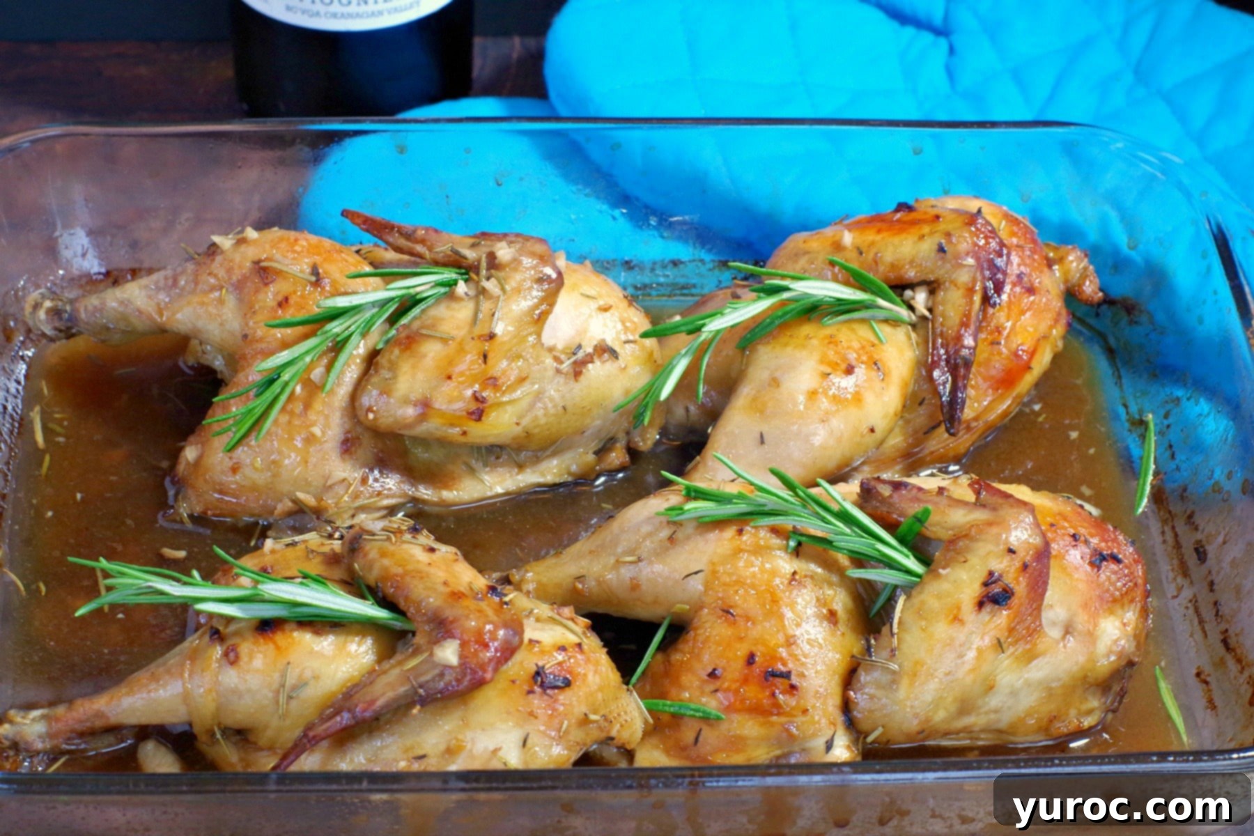 Two golden-brown Cornish hens, cooked with a savory wine sauce, presented in a clear glass baking dish, ready to be served.