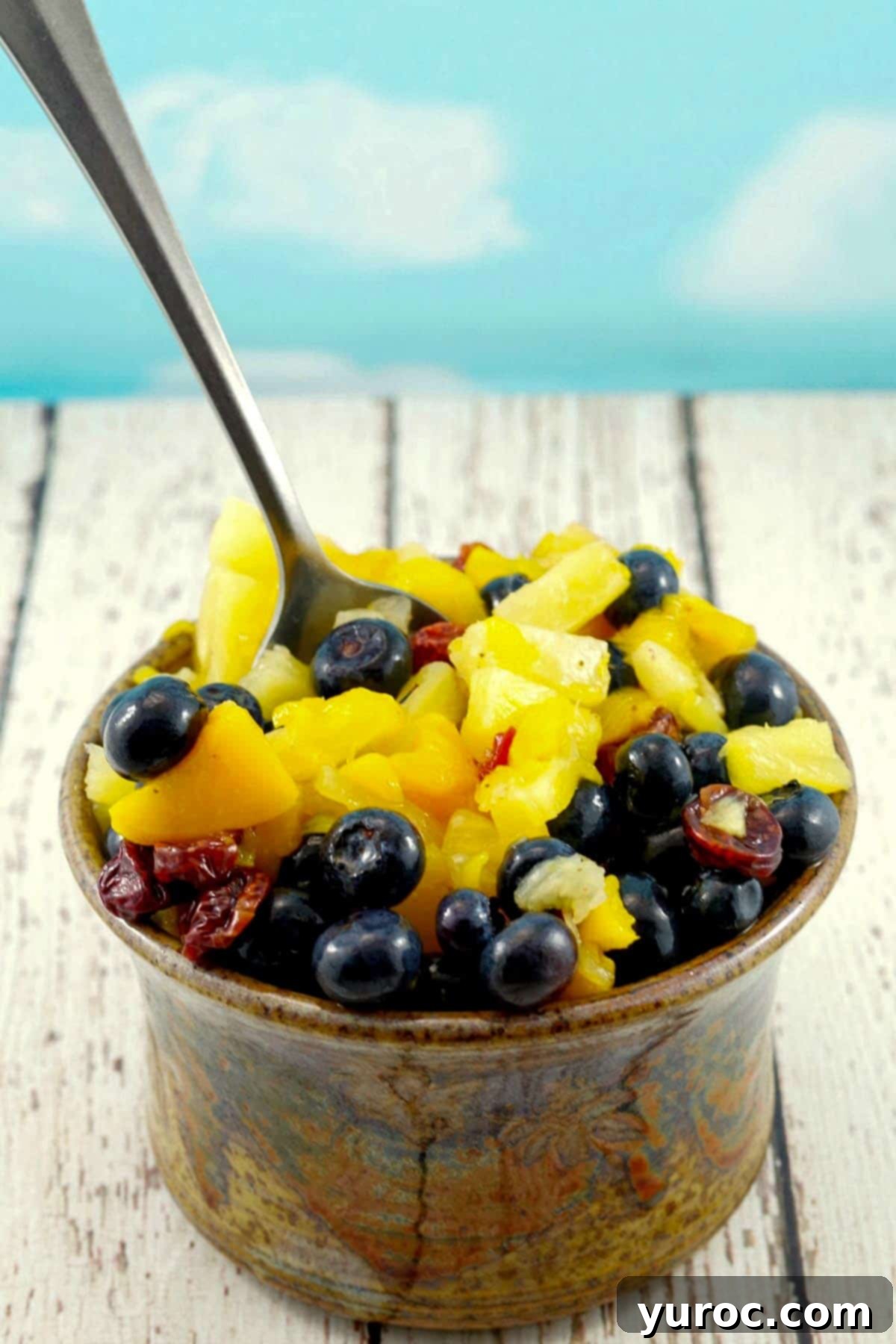 Sun-Kissed Peach Pineapple Salsa 4 pineapple peach fruit salsa in a brown dip bowl with a serving spoon, on a white faux wood surface