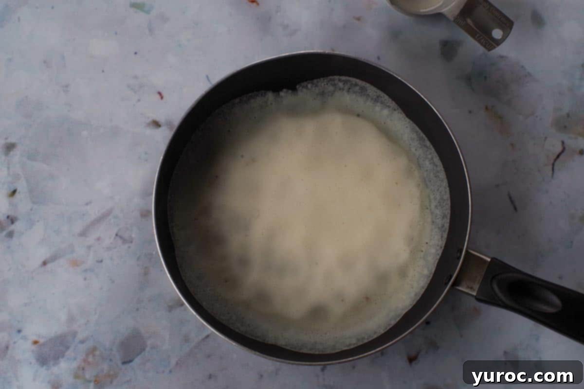 Crepe batter being poured into an 8-inch frying pan.