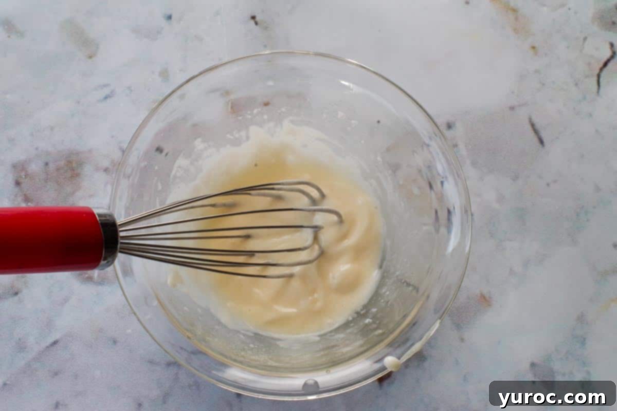 Zesty Artichoke Red Bell Pepper Slaw 4 Dressing ingredients being mixed together in a glass bowl with a small whisk.