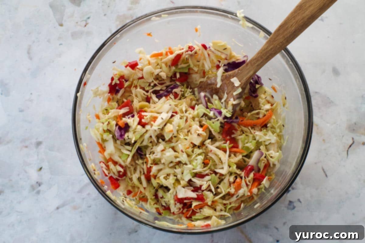 Zesty Artichoke Red Bell Pepper Slaw 6 Artichoke & Roasted Red Bell Pepper Coleslaw ingredients mixed together in a large glass bowl, with a wooden spoon.