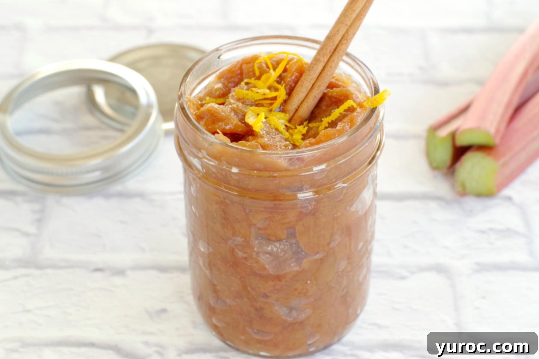 Homemade rhubarb compote in a glass jar, garnished with a cinnamon stick and fresh orange zest, ready to be served or stored.