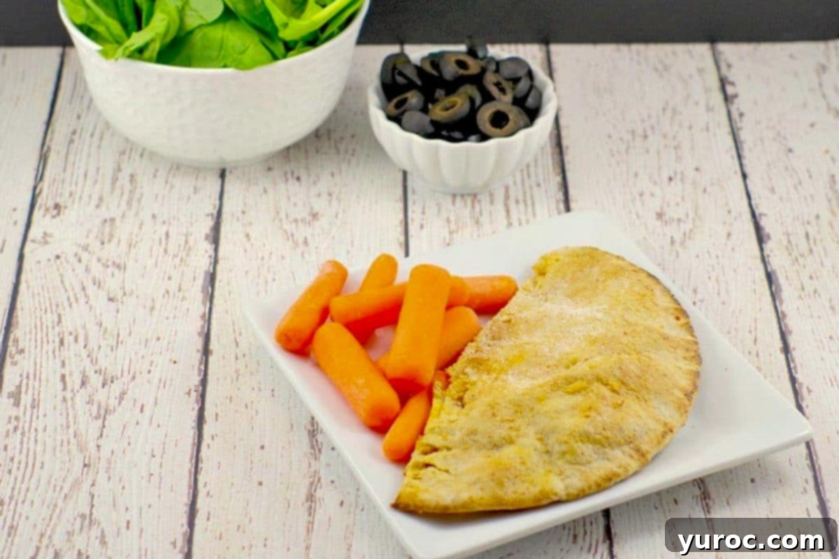 Wholesome Pita Pizza Pouches 2 A healthy pizza pocket on a white plate with baby carrots and a dish of olives and spinach in the background, showcasing its delicious filling.