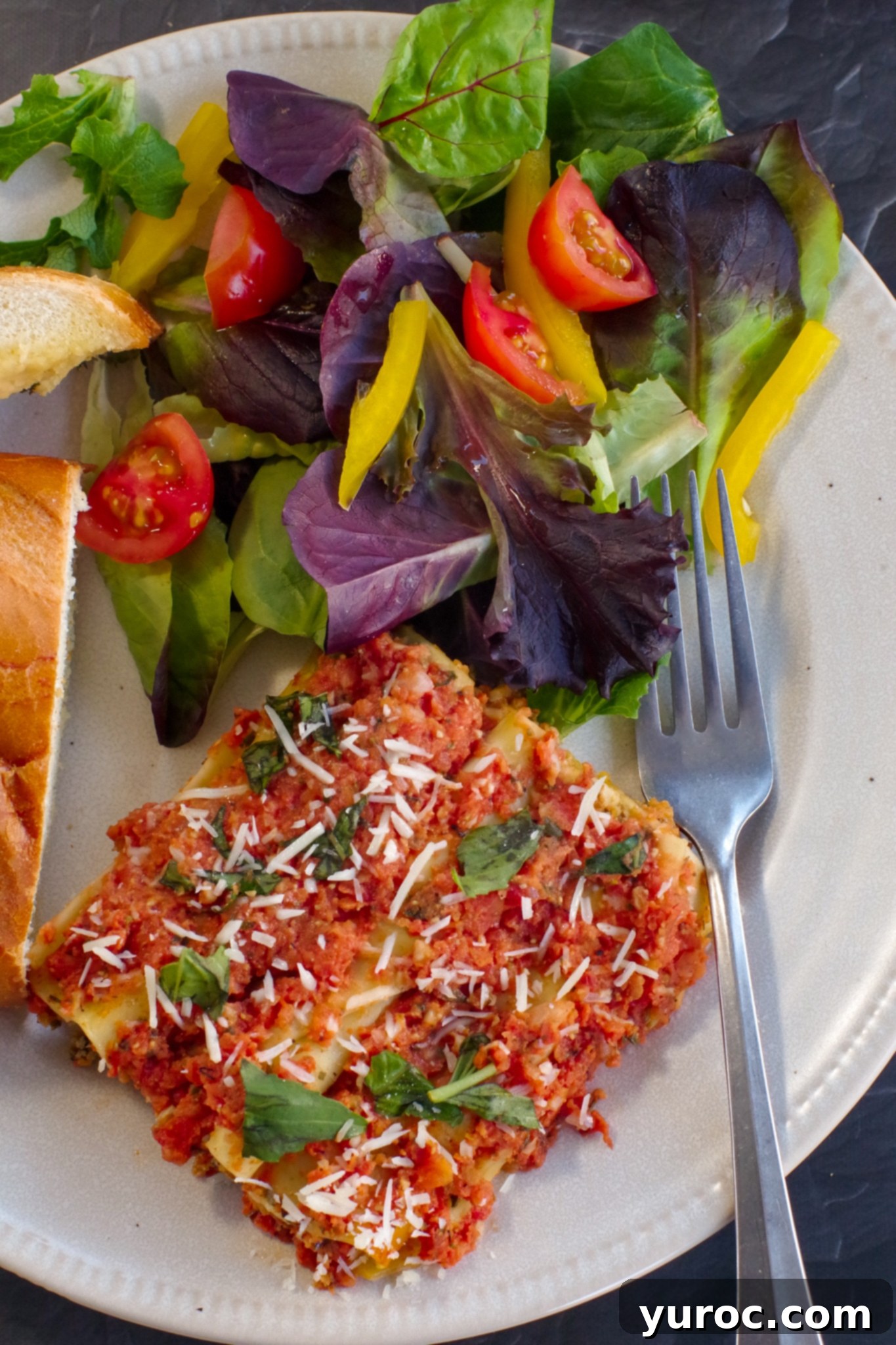 baked beef cannelloni on plate with garlic toast and garden salad, garnished with fresh basil