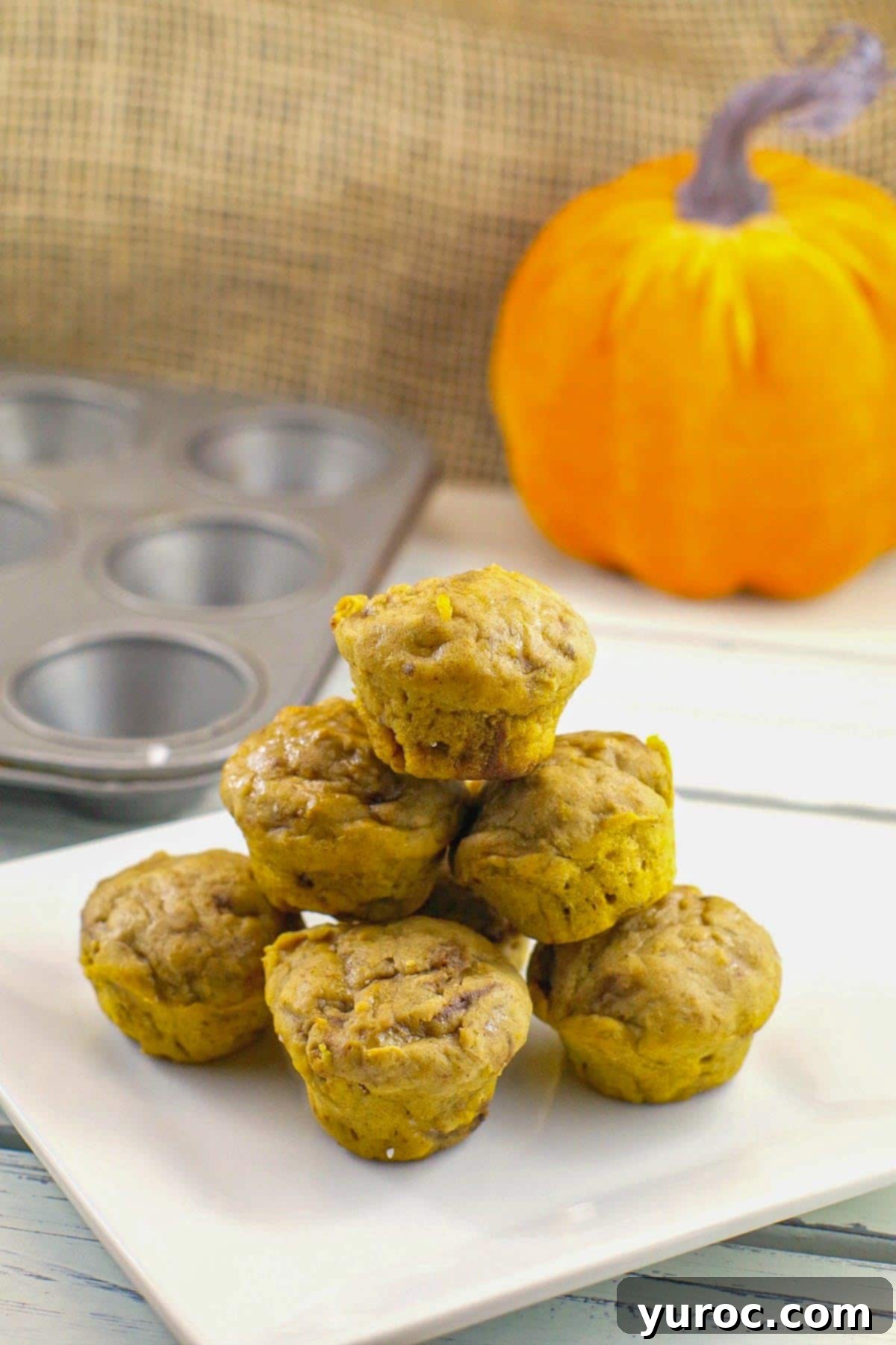 healthy pumpkin pie blondies stacked on a white plate with mini muffin tin and pumpkin prop in the background