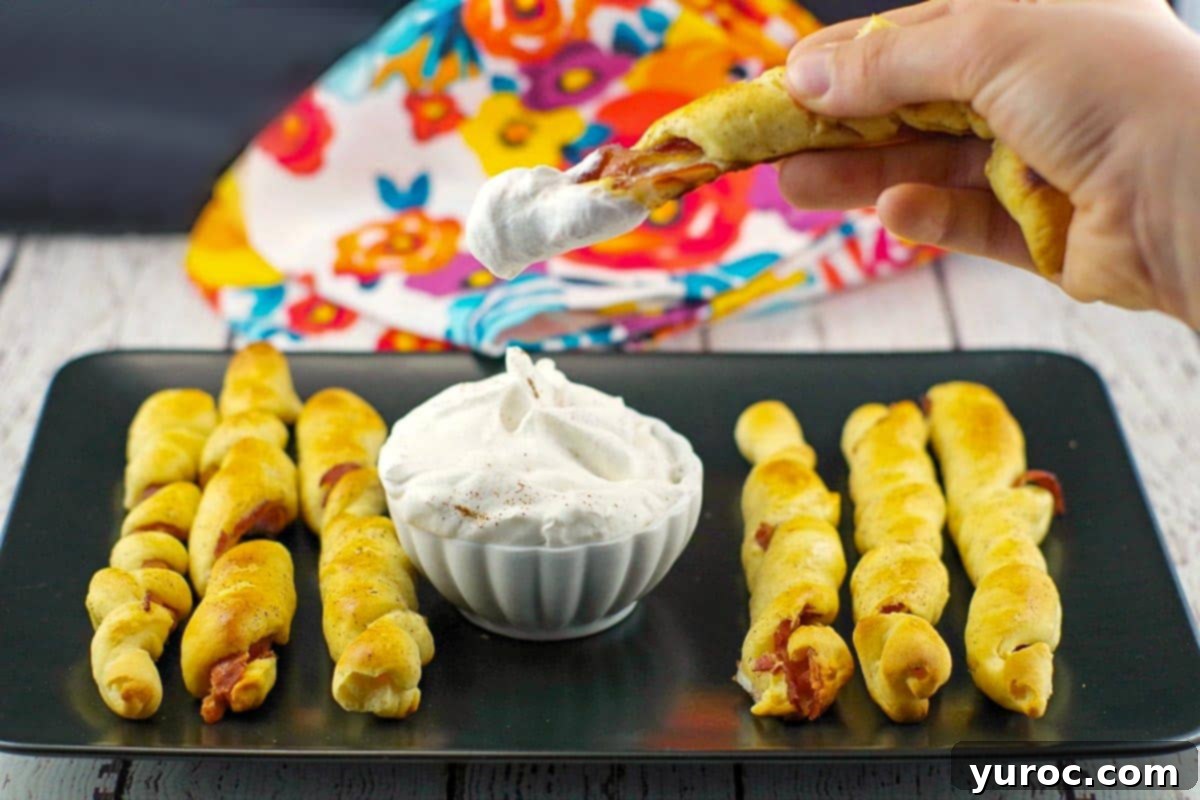 French Toast Sausage Rolls 2 breakfast pigs in a blanket on black tray with dip in the middle and one being dipped into dip