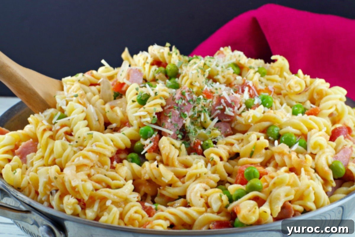 Healthy Ham Pasta in a skillet with a wooden spoon, with a red napkin in the background.