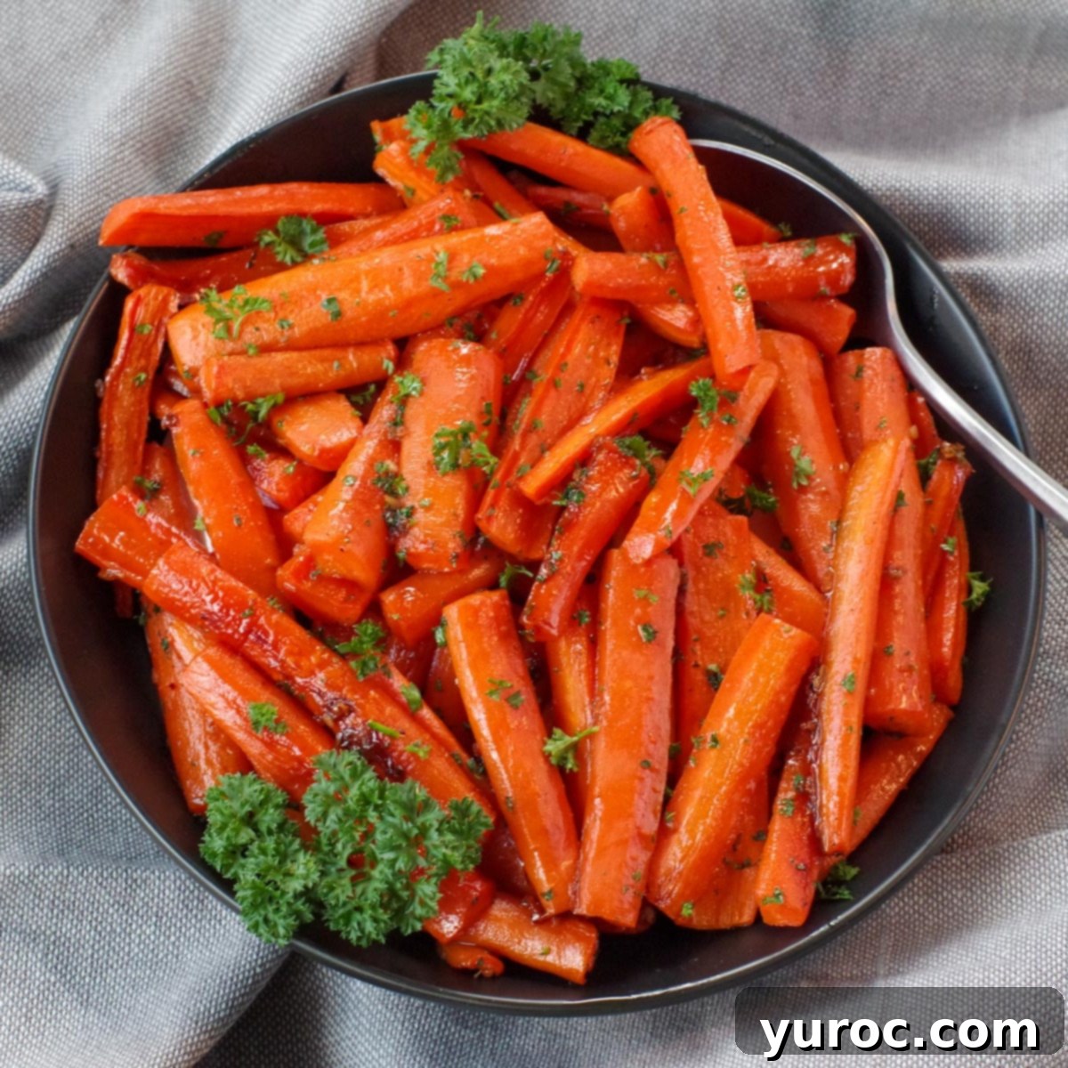 brown sugar glazed carrots in a black bowl, with a spoon, on grey linen