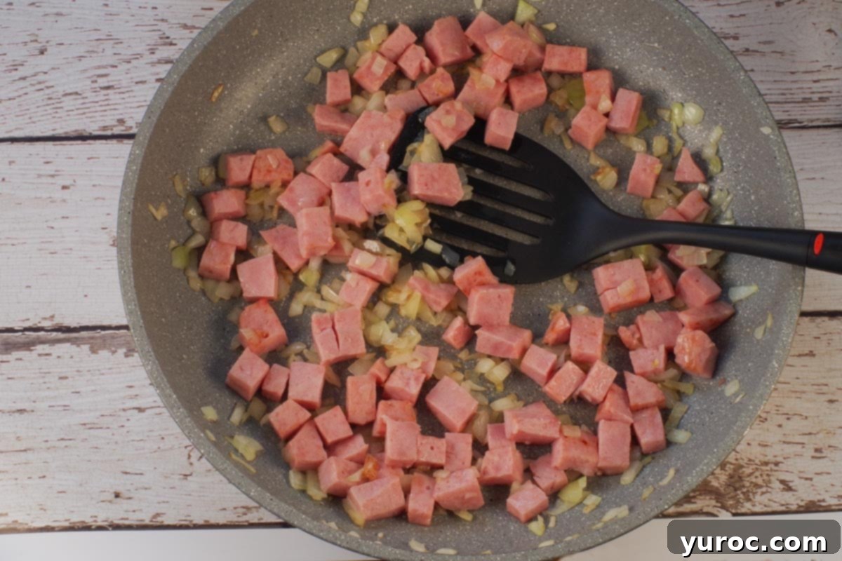 Cubed ham and onions in skillet with black spatula.