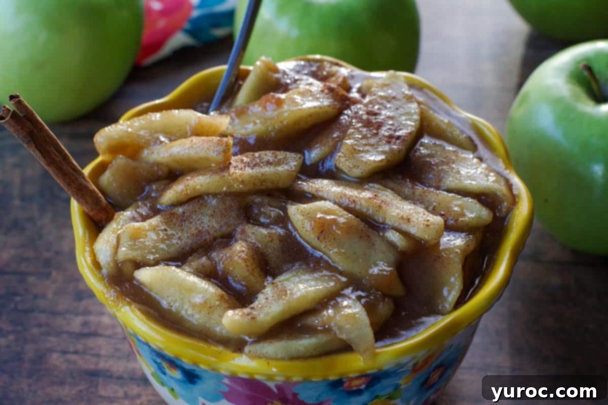The Perfect Award-Winning Apple Pie Recipe 11 stovetop apple pie filling in a flowered blue bowl with yellow rim, with spoon and cinnamon stick in it