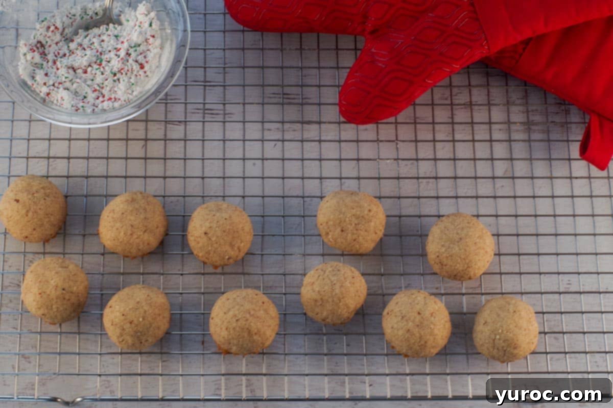 Winter Spice Almond Snow Puffs 11 Baked Snowball Cookies on a Cooling Rack with red oven mitts in background.