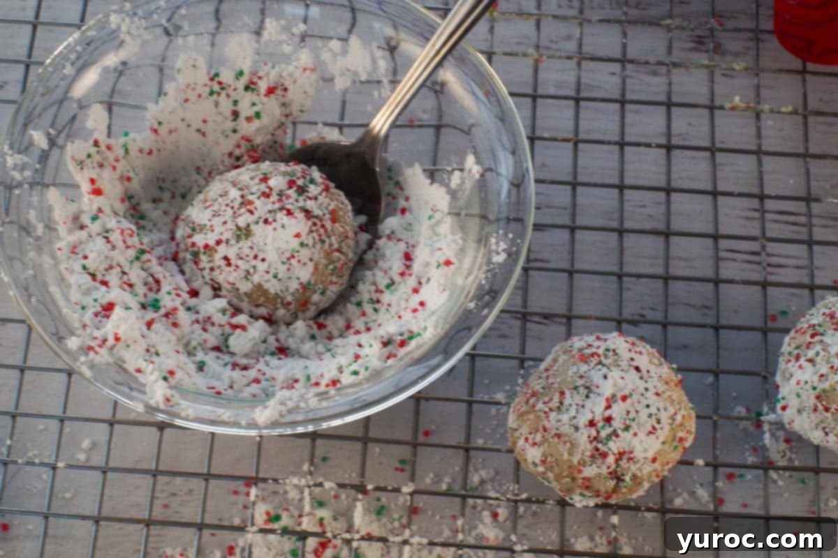 Winter Spice Almond Snow Puffs 13 An almond snowball cookie being rolled in powdered sugar and sparkling sugar mixture.