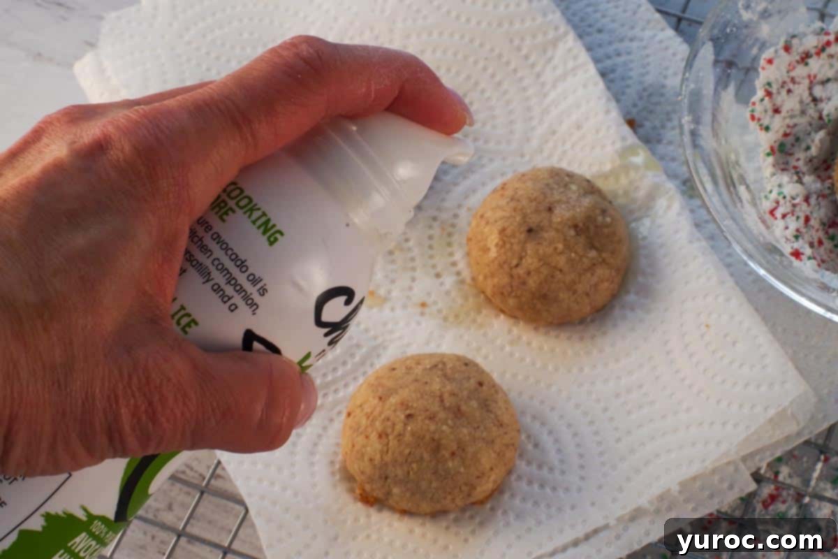 Winter Spice Almond Snow Puffs 14 Oil being sprayed on almond snowball cookies to help the powdered sugar stick better.