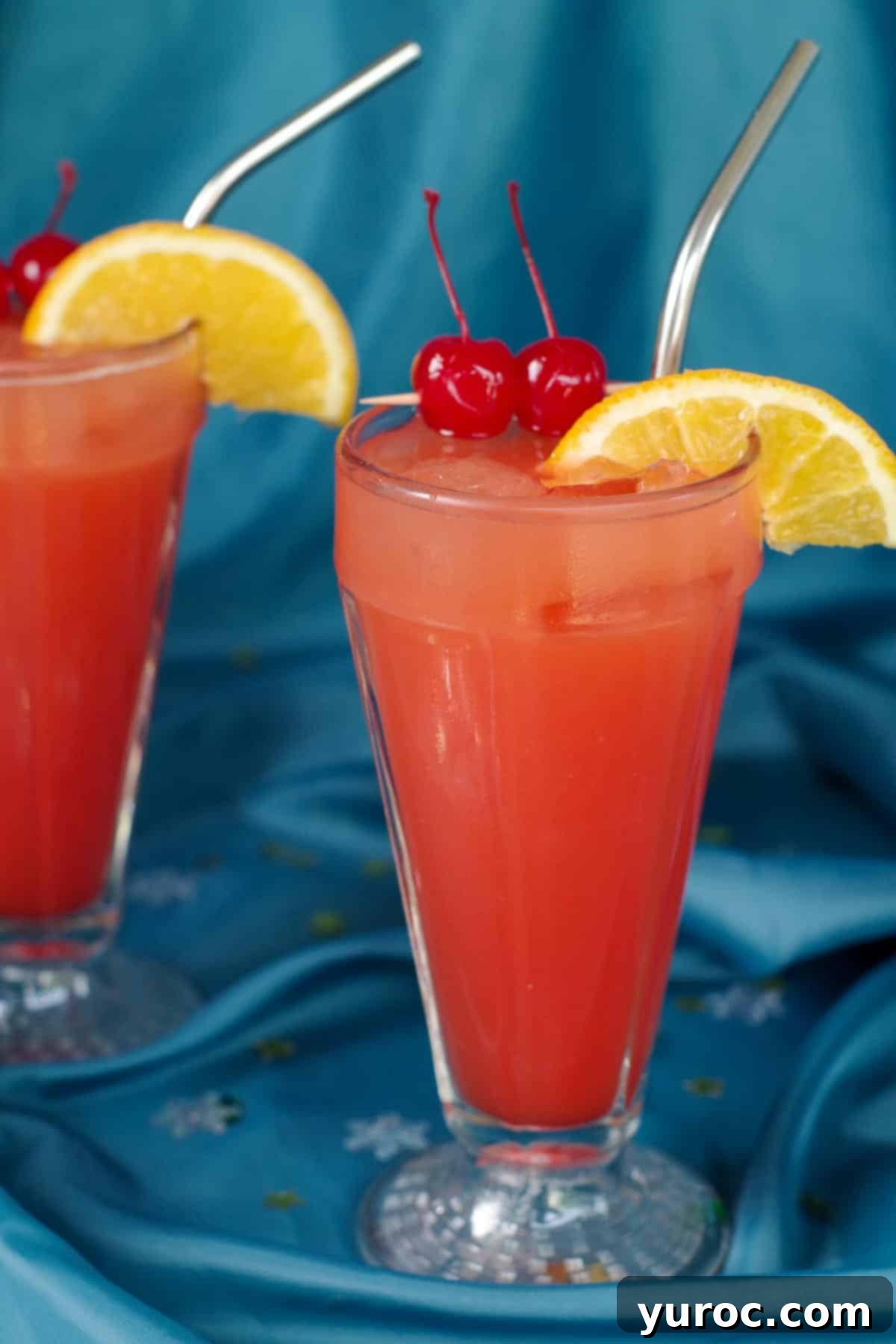 Shirley Temple Mocktail Recipe 2 Two glasses of Shirley Temple drinks on a vibrant blue fabric surface, ready to be enjoyed.