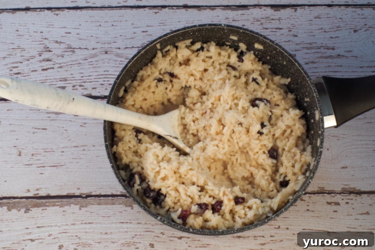 All ingredients in rice pudding cooked in pot with large spoon.