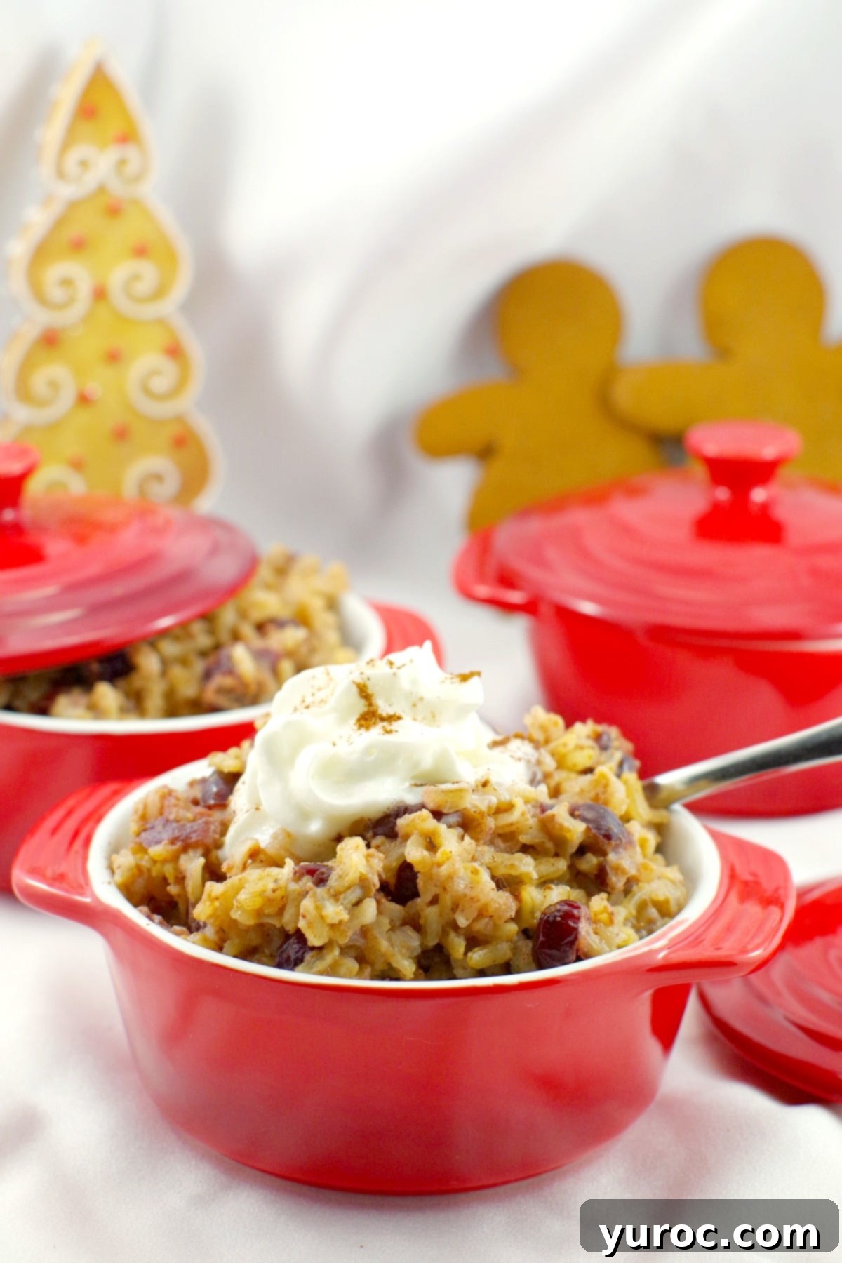 Cranberry Gingerbread pudding in a red bowl with more red bowls in the background and a gingerbread tree and gingerbread men