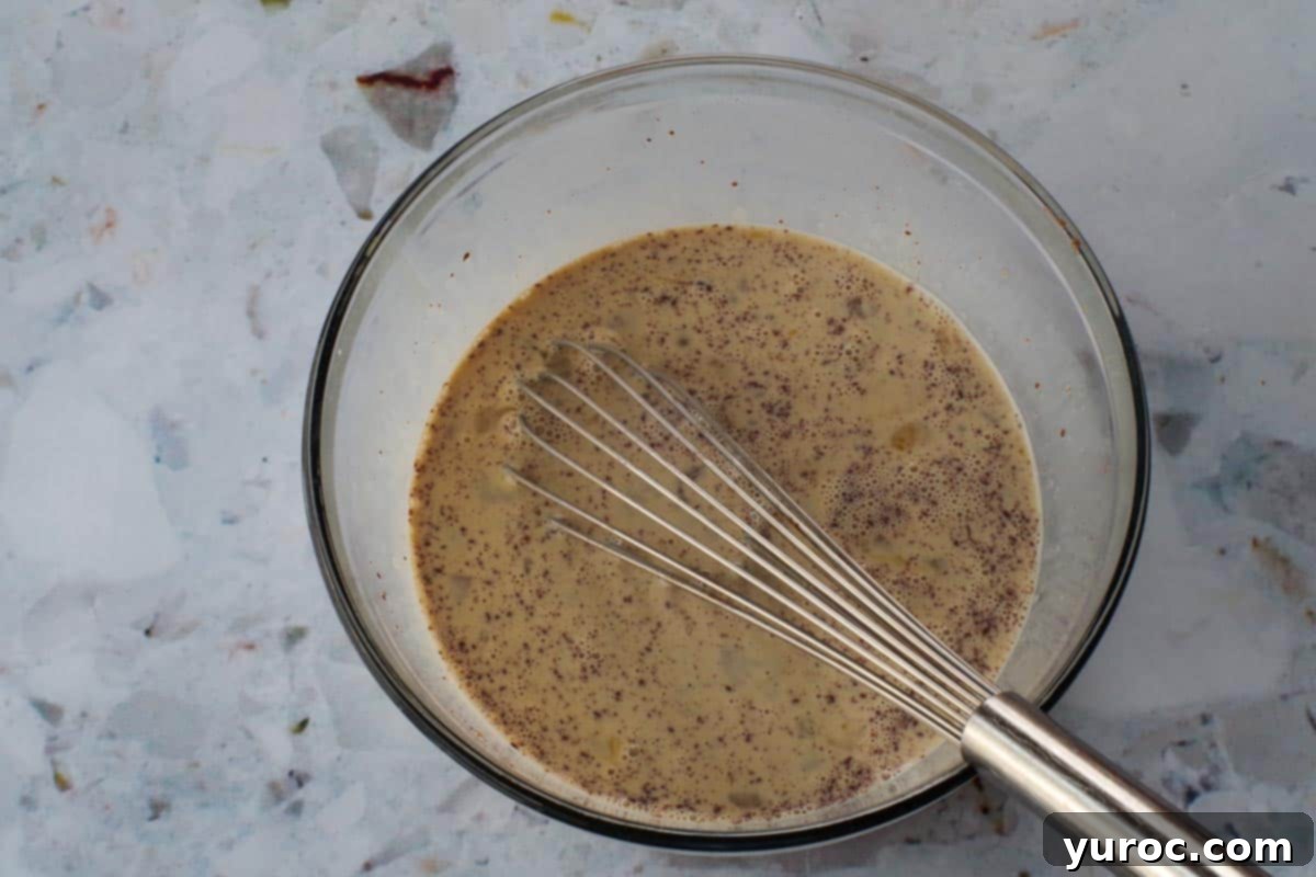 Liquid ingredients whisked together in large glass bowl with metal whisk.
