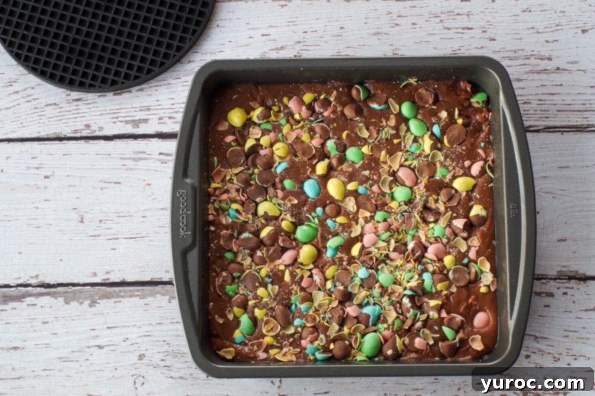 Crushed Cadbury Mini Eggs sprinkled generously on top of the fudge mixture in the pan and gently pressed in, creating a colorful and textured topping.