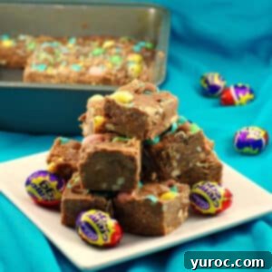 Squares of Easter Creme egg fudge piled on a white plate with a pan of fudge in the background