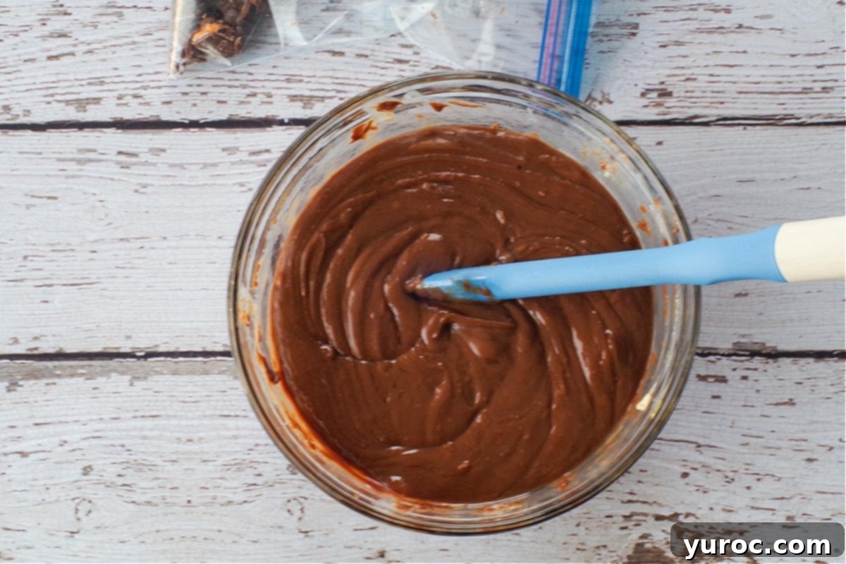 Microwaved chocolate mixture in a glass bowl, now melted and smooth, being stirred with a spatula to ensure full incorporation.