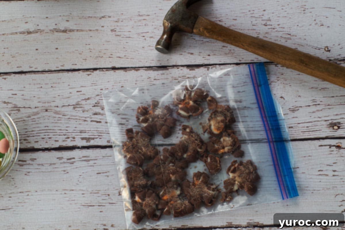 Cadbury Mini Creme Eggs crushed in a Ziploc bag next to a hammer, demonstrating the method for preparing them.