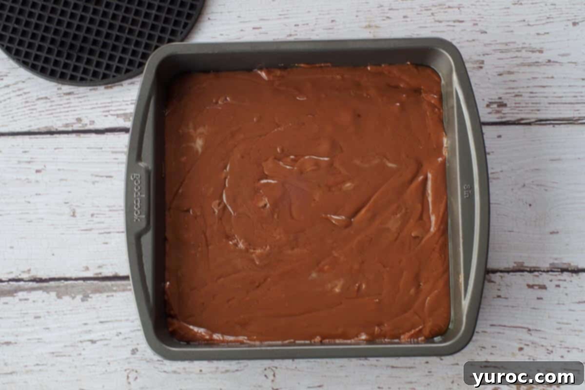 The smooth fudge mixture, infused with crushed Creme Eggs, transferred and spread evenly into a square prepared pan, ready for chilling.
