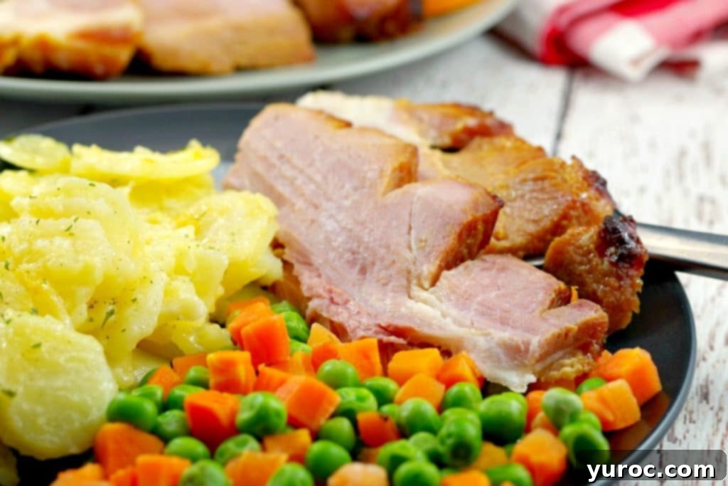 Sliced picnic ham on a plate with scalloped potatoes and veggies with whole ham in background