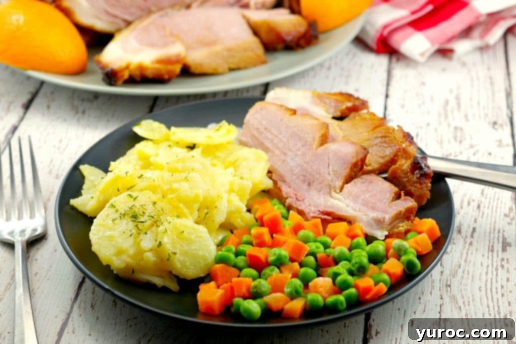 Sliced picnic ham on a plate with scalloped potatoes and veggies with whole ham in background