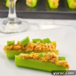 2 buffalo chicken celery sticks on a white plate with a glass of wine and a black platter with more celery sticks in background