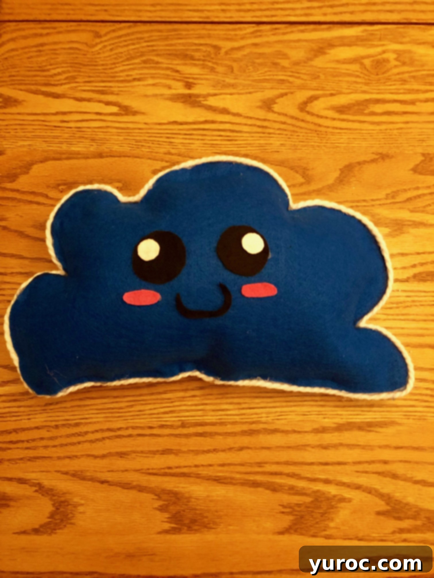 Blue stuffed cloud pillow with white lining and a smiley face and pink cheeks