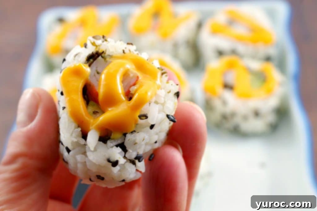 Close up of California Roll with swirl of sriracha mayonnaise on top and additional rolls in the background