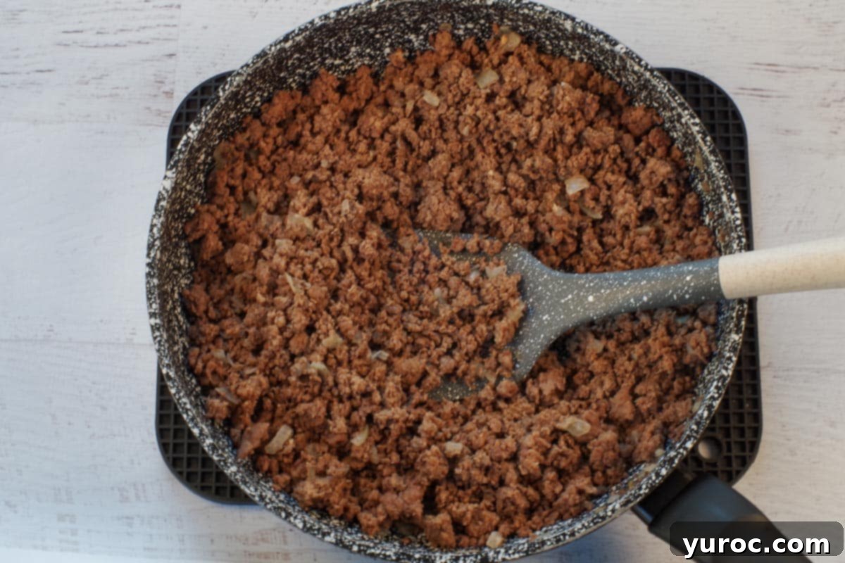 Ground beef and chopped onions cooking in a large frying pan with a spatula