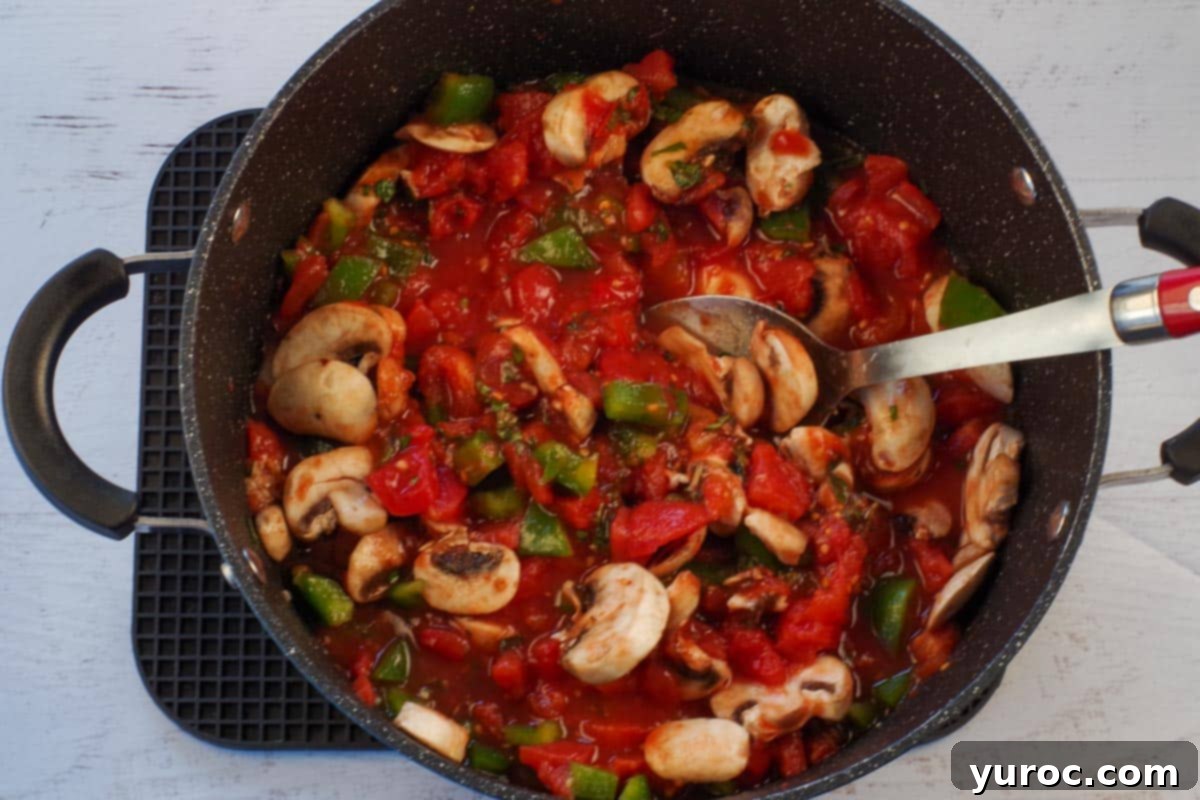 Tomato base mixture cooking in a large pot with a wooden spoon