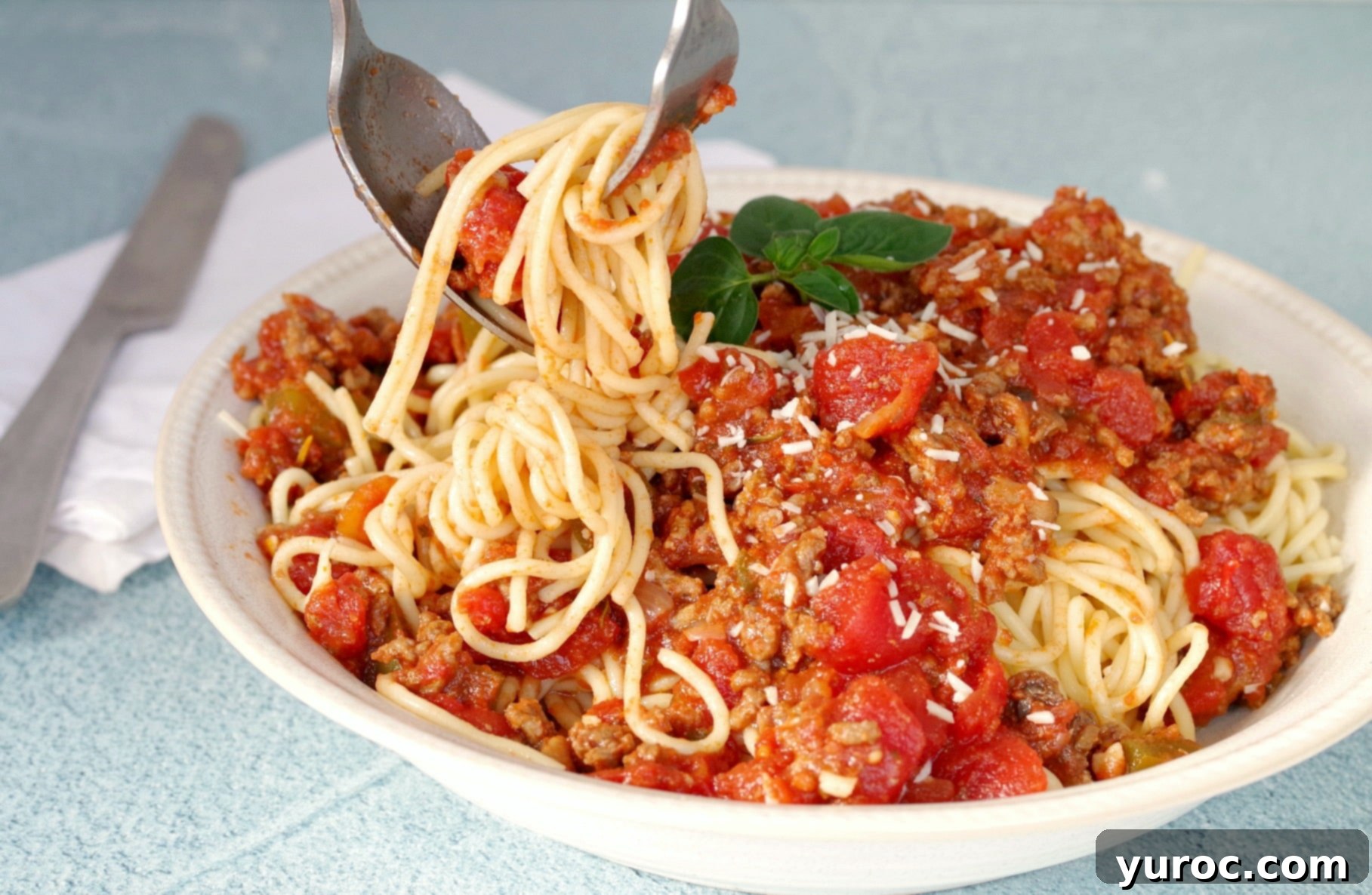A fork twirling spaghetti with meat sauce, garnished with fresh herbs, against a rustic background